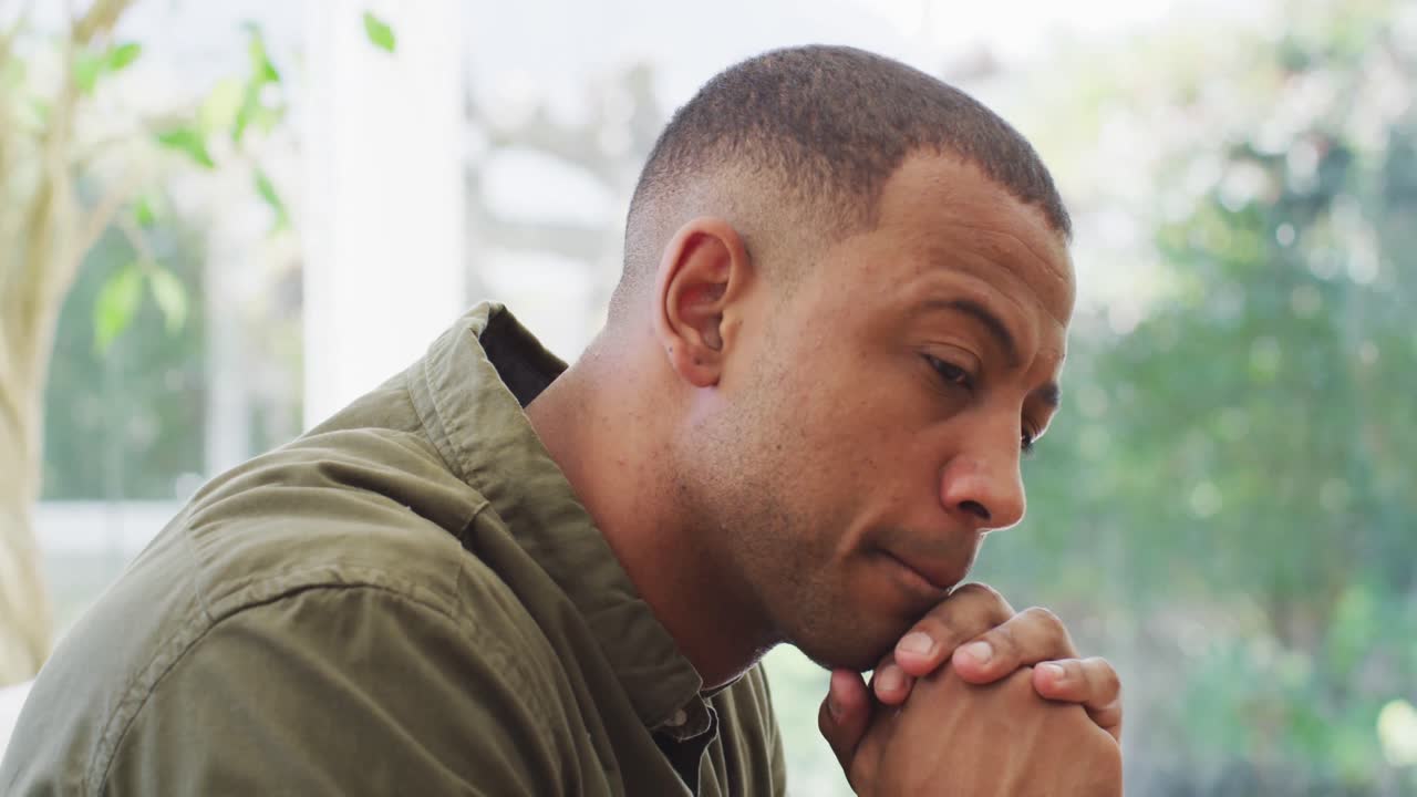 Retrato de homem birracial pensativo sentado no sofá e virando-se