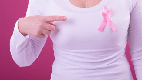 video of midsection of caucasian woman wearing pink cancer awareness ribbon, with pink background