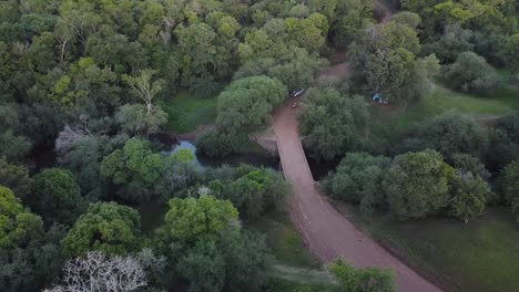 Aerial-pullback-tilt-up-reveals-river,-bridge,-and-forest-split-shadow-and-light