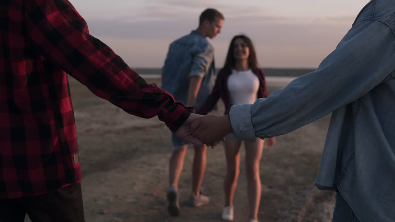 pareja feliz de hombre y mujer caminando y tomados de la mano en una playa desierta con el cielo al anochecer. dos parejas caminando al aire libre. cultura juvenil. jóvenes felices