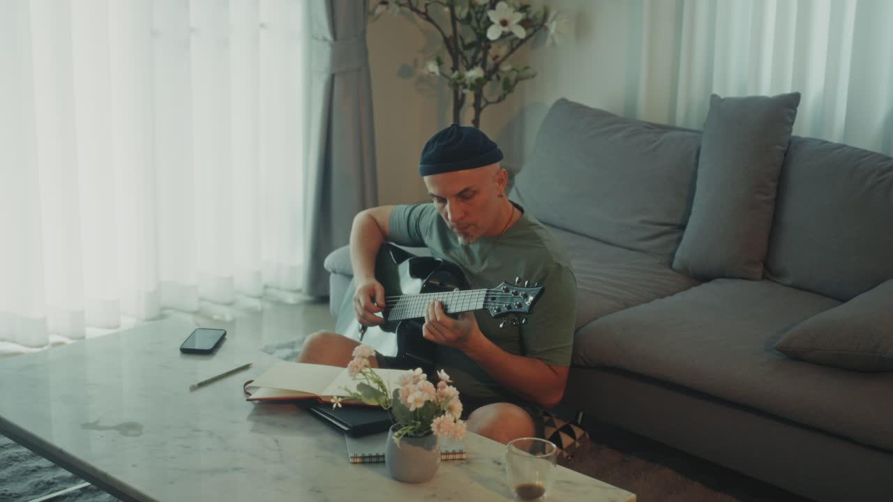 Man Playing Acoustic Guitar and Composing Music at Home