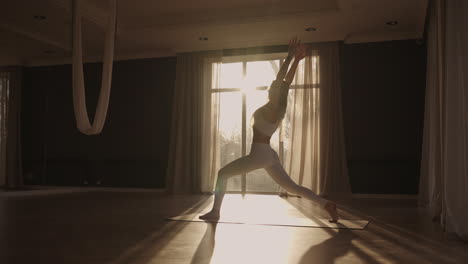 slow motion: young woman is doing yoga in a white room filled with light the girl performs yoga stands and elements near the large window.