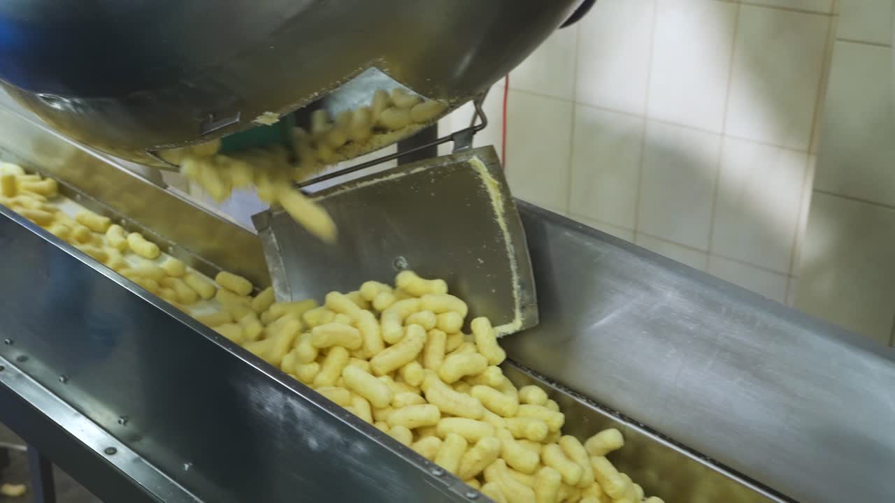 Produção de palitos de milho doces glaçados. Esteira transportadora de metal com snacks em uma fábrica de alimentos