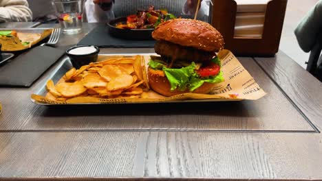 disparo en primer plano de una hamburguesa de carne jugosa con lechuga y una rebanada de tomate con un lado de papas fritas frescas, sentado en un plato en el restaurante, ampliando