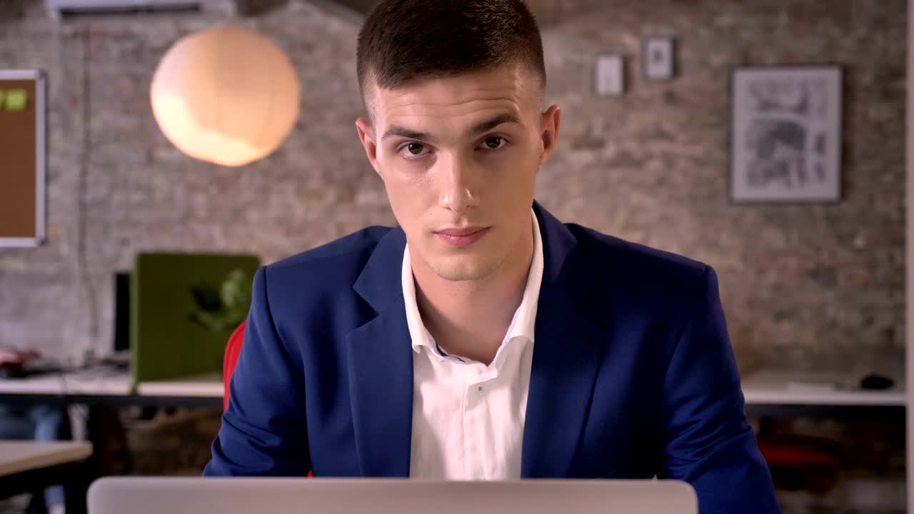 молодой красивый бизнесмен смотрит в ноутбуке, смотрит в камеру, коммуникационная концепция, бизнес-концепция