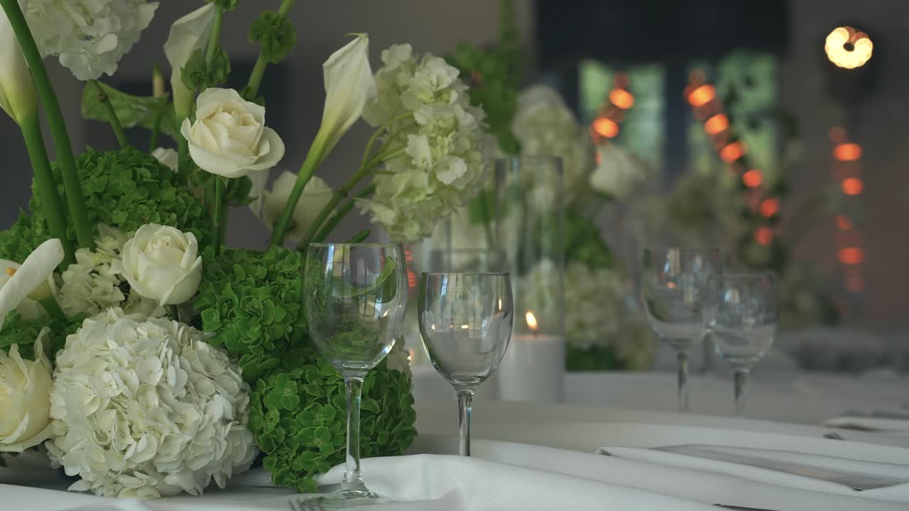 Elegant wedding reception table decorated with lush white and green floral arrangements, glassware, and candles, creating a luxurious and romantic ambiance for a special celebration