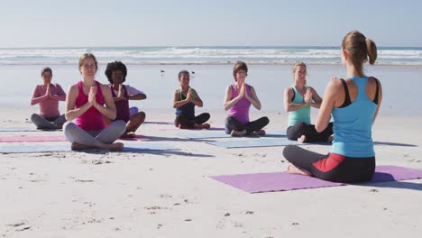 multi-ethnic group of women doing yoga and gathered hands on the beach and blue sky background