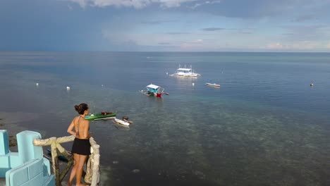 Woman-looks-out-from-tower-over-calm-Philippines-sea,-fly-by-drone-shot