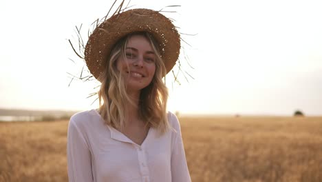Attractive,-Funny,-Smiling-Blonde-Woman-In-White-Shirt-And-Straw-Hat-Posing-While-Walking-By-Wheat-Field-On-Sunny-Summer-Day