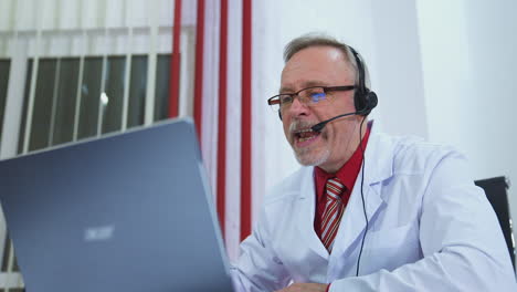 doctor in surgery office with headphones in front of his laptop. telemedicine concept