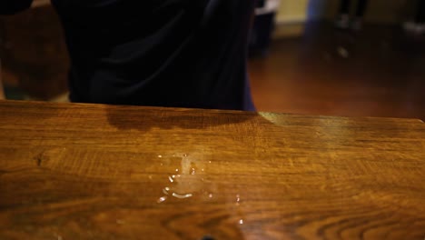 un hombre derrama cerveza en una mesa de madera.