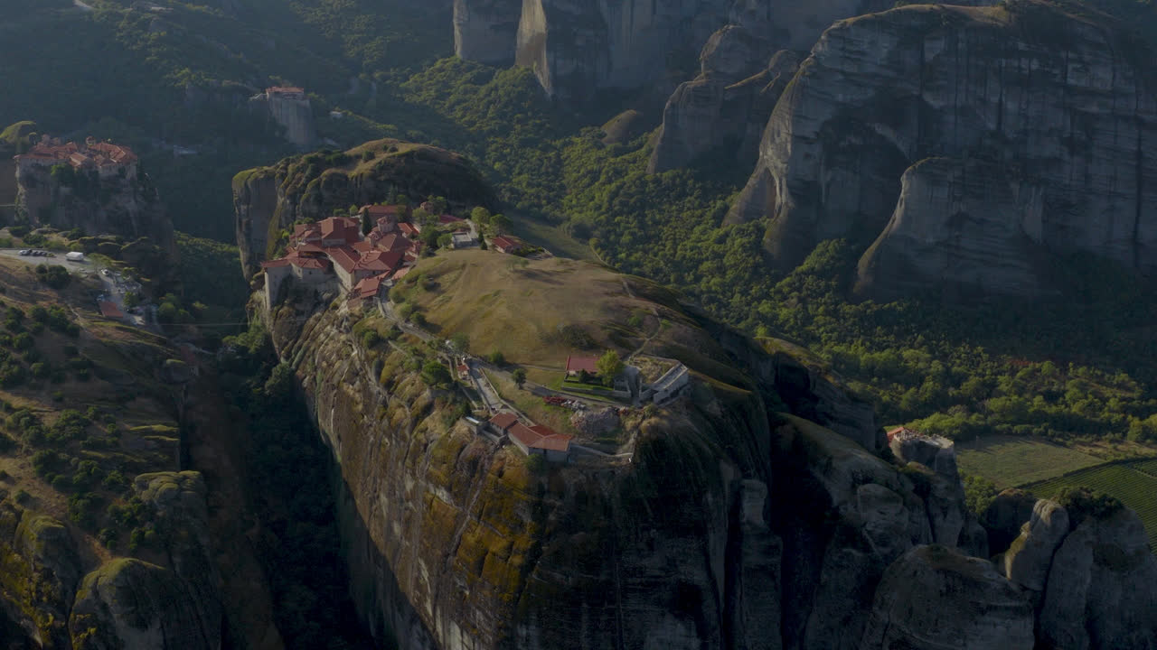 Cinematic aerial view of Meteora monastery in Greece perched on towering cliffs, dramatic rock formations and lush green valley create a breathtaking historic scene