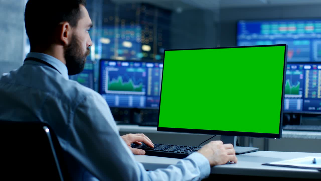 comerciante del mercado de valores que trabaja en una computadora con una pantalla verde de maqueta aislada. en el fondo los monitores muestran números y gráficos de cotización de acciones.