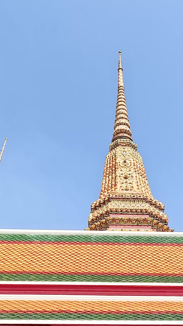 Una vista serena della pagoda di Wat Pho contro un cielo azzurro brillante a Bangkok, che mostra l'architettura tradizionale thailandese e colori vivaci.