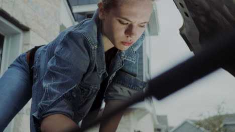 woman in early 20s checking under the hood of a truck and going under the truck to find and fix mechanical problem