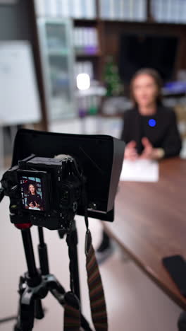 professional camera with display filming a caucasian brunette sitting at desk. close up. creation of content for internet blog. vertical video.