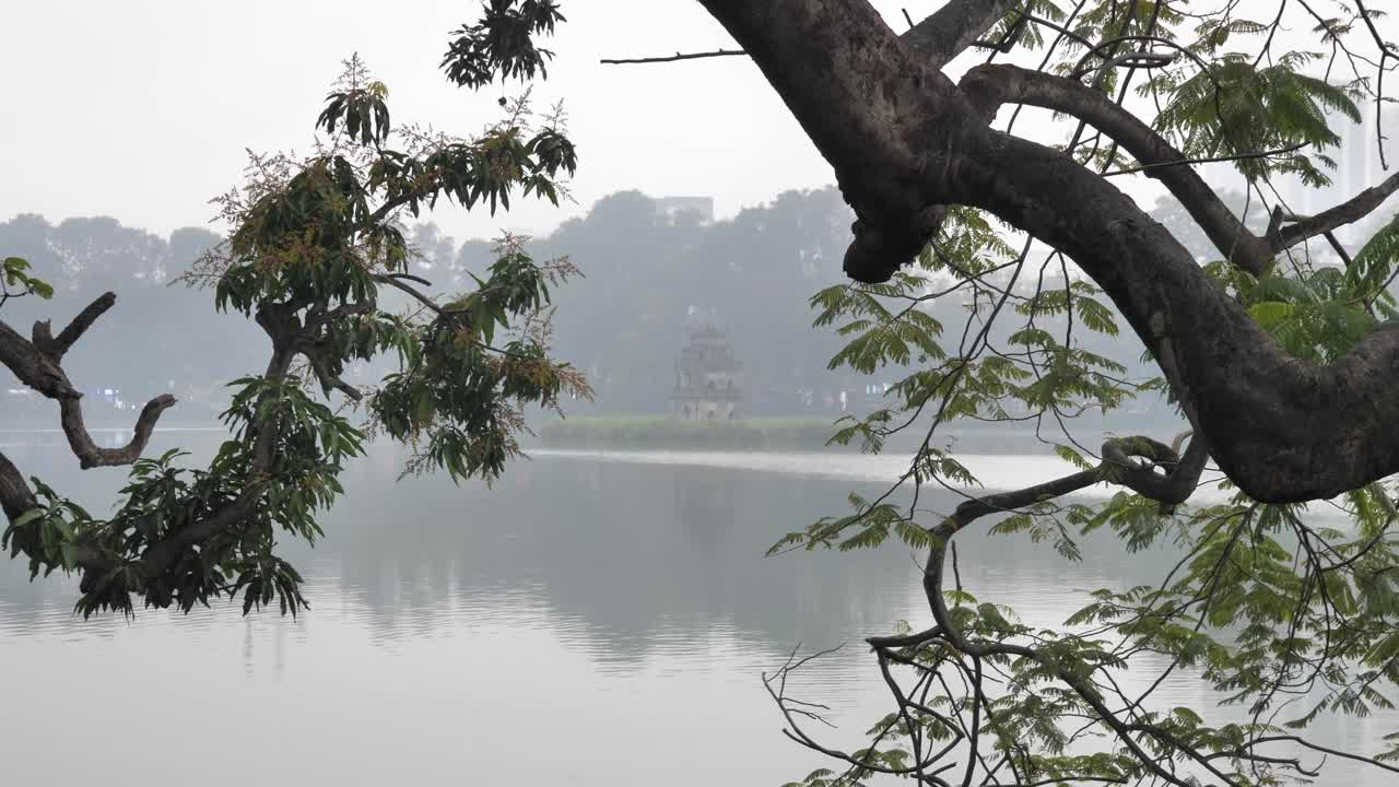Turtle Tower in the middle of Hoan Kiem Lake with a tree and fog during the day in Hanoi, the capital city of Vietnam, wide shot