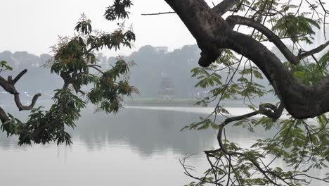 turtle tower in the middle of hoan kiem lake with a tree and fog during the day in hanoi, the capital city of vietnam, wide shot