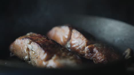 2 filetes de salmón cocinando y chisporroteando en una sartén - primer plano