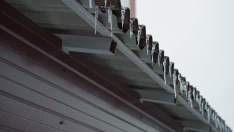 close-up of roof edge covered in frosted ice and hanging icicles, showcasing intricate frozen textures along the metal structure, set against a bright wintery sky and minimalistic background