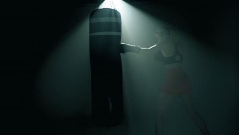 blonde woman in full view powerfully punches a heavy black boxing bag with large black gloves. cinematic backlight highlights her silhouette in smoky gym as camera slowly pushes in toward her