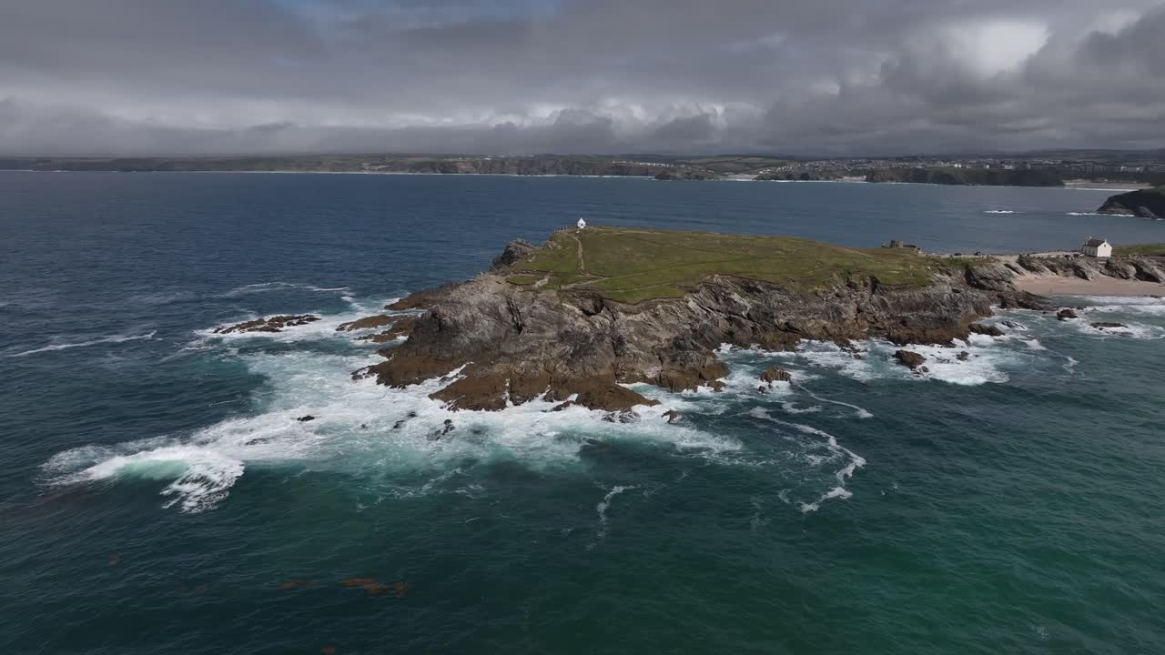 Ilmakuva, joka kaareutuu Towan Headlandsin ympäri Newquayssa suurten maininkien ympäröimänä.
