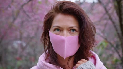woman wearing pink mask in cherry blossom trees