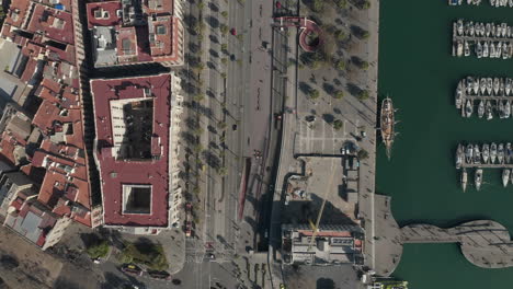 Top-down-footage-of-traffic-on-streets-along-town-port-with-moored-yachts-and-sailboats.-Barcelona,-Spain