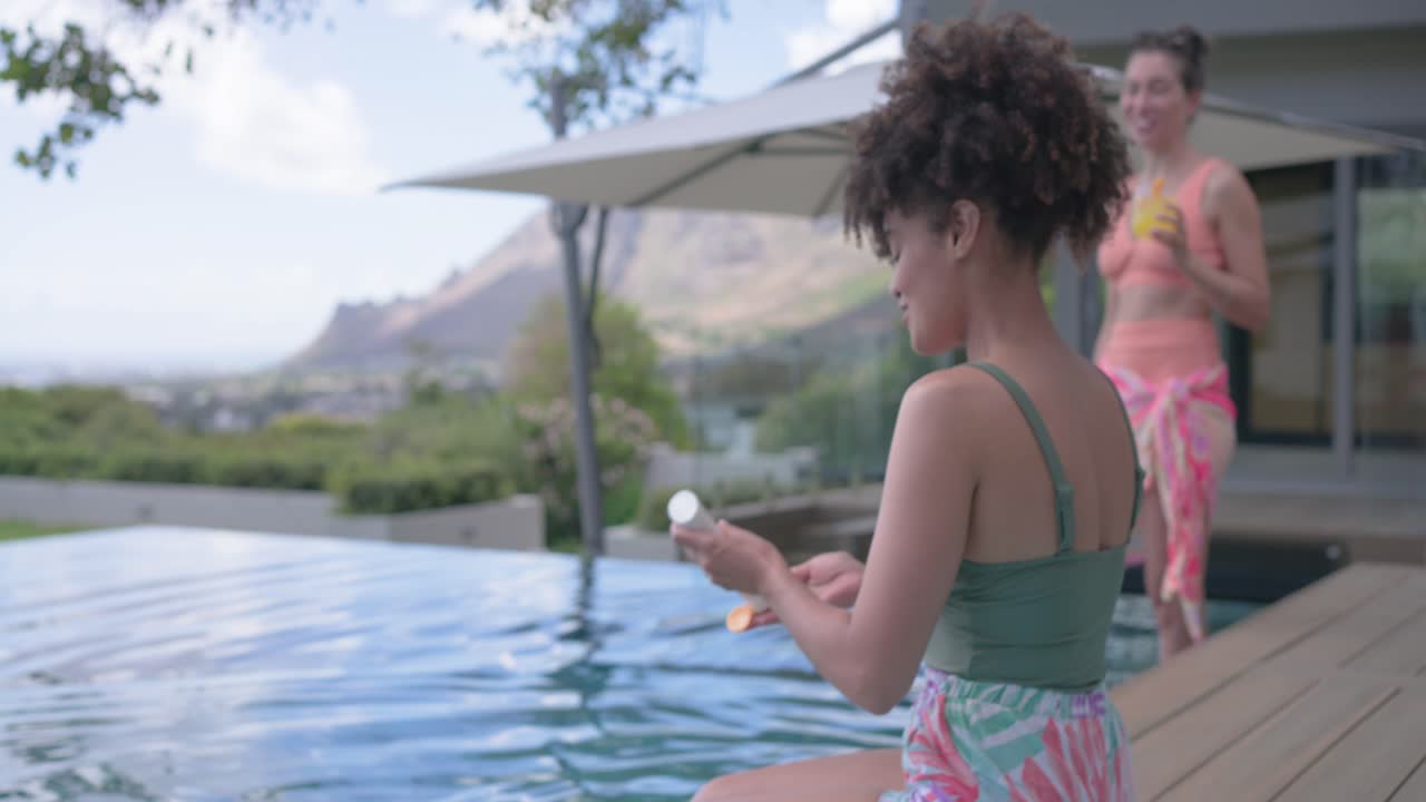 Verschiedene Frauen stehen an einem Infinity-Pool, eine nippt an einem Getränk, die andere trägt Sonnencreme zum Sonnenschutz auf.