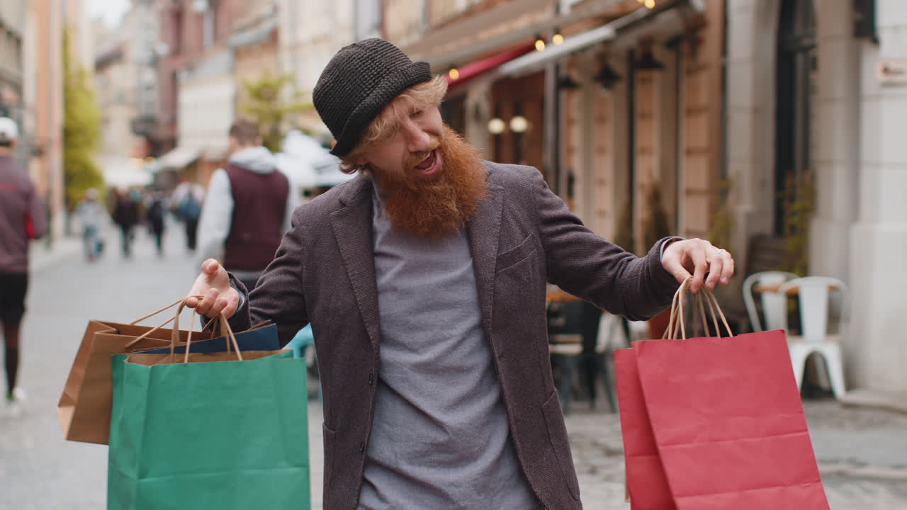 Happy young man shopaholic consumer after shopping sale with full bags walking in city street
