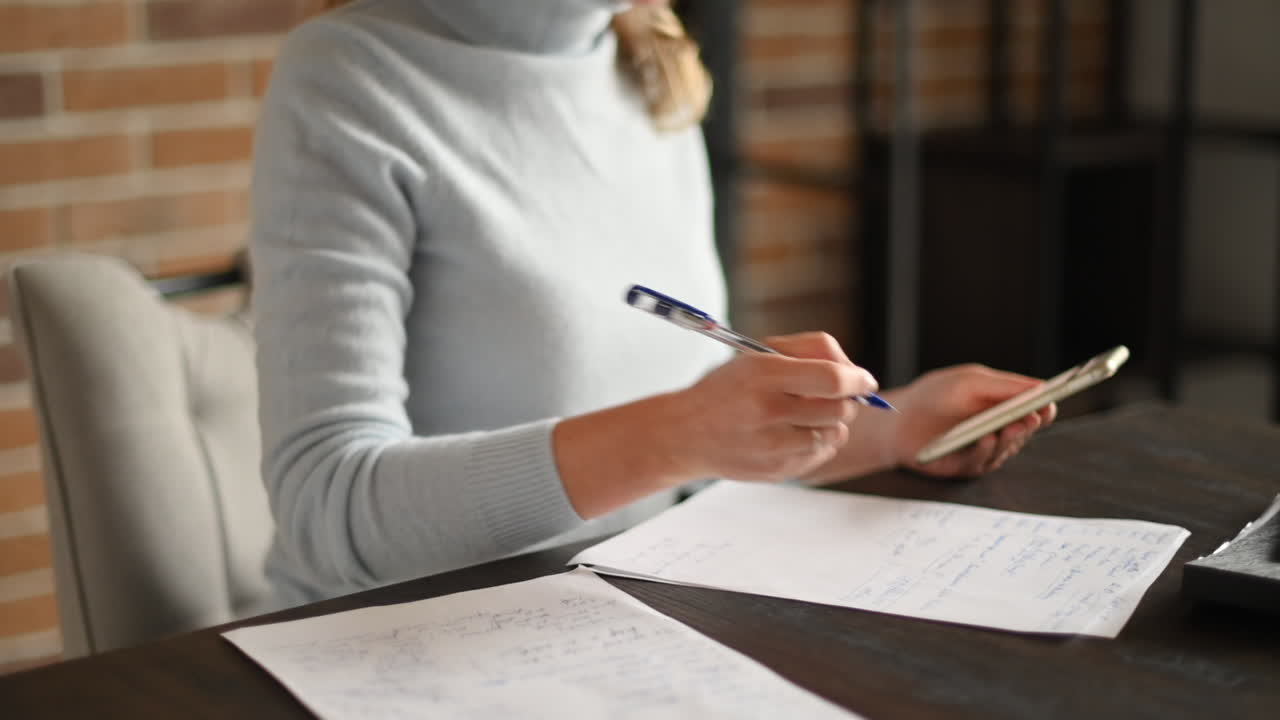 Woman working on mobile phone and writing at the office