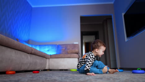 adorable smiling baby boy rolls the rings from toy pyramid. lovely happy toddler plays cheerfully at home.
