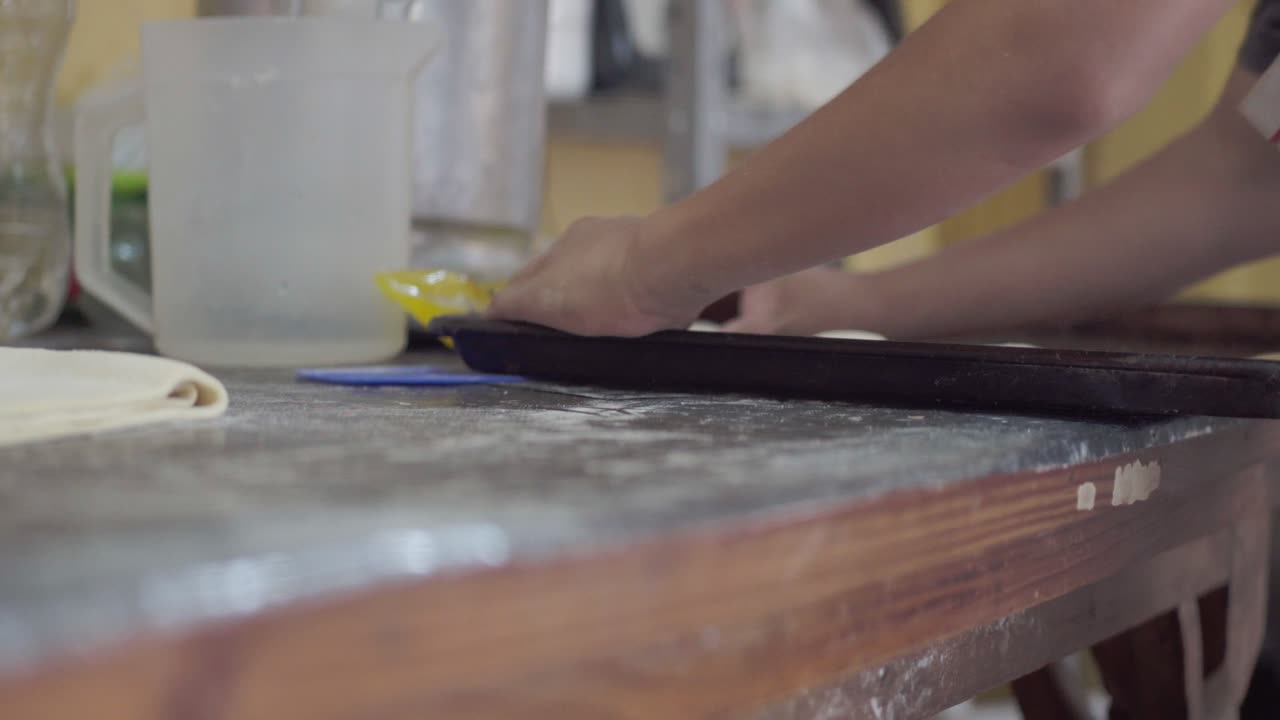 A baker carefully places dough onto a baking sheet in a bakery for preparation.