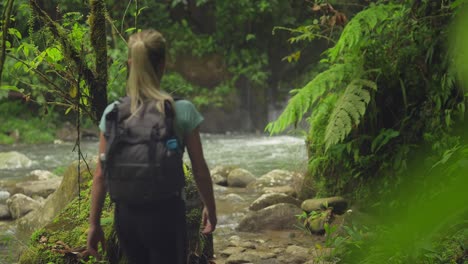 sportive blond female tourist with backpack walking in tropical river valley