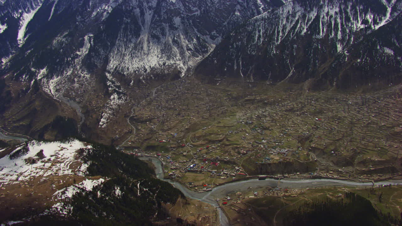 vista aérea sobre montañas cubiertas de nieve hasta un valle con casas coloridas, estilo de vida, río y bosque que crean una vista pintoresca