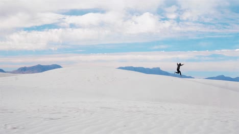 slow motion shot of a man running and jumping off of a large sand dune in the famous white sands national monument park in new mexico on a bright sunny summer day
