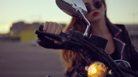 portrait of a female biker in leather jacket and shorts sitting on her bike and holding a handlebar. close up of young sexy