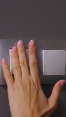primer plano de la mano de la mujer presionando el interruptor de la luz en una habitación débilmente iluminada, el brillo ambiental suave resalta los dedos mientras enciende la luz, creando un contraste entre la oscuridad y la iluminación