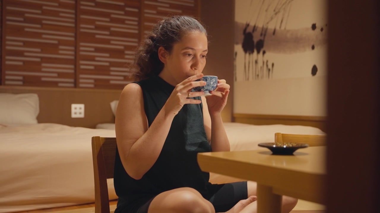 Young caucasian woman sitting cross legged at a low table in a traditional Japanese room, smelling and savoring a cup of authentic green tea, enjoying a moment of tranquility and mindfulness