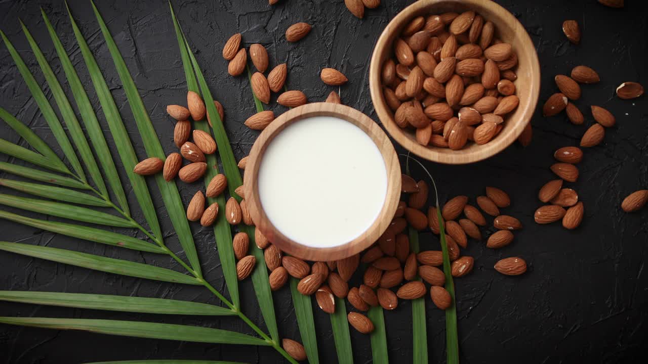 semillas de almendras en cuenco de madera leche natural fresca colocada sobre fondo de piedra negra