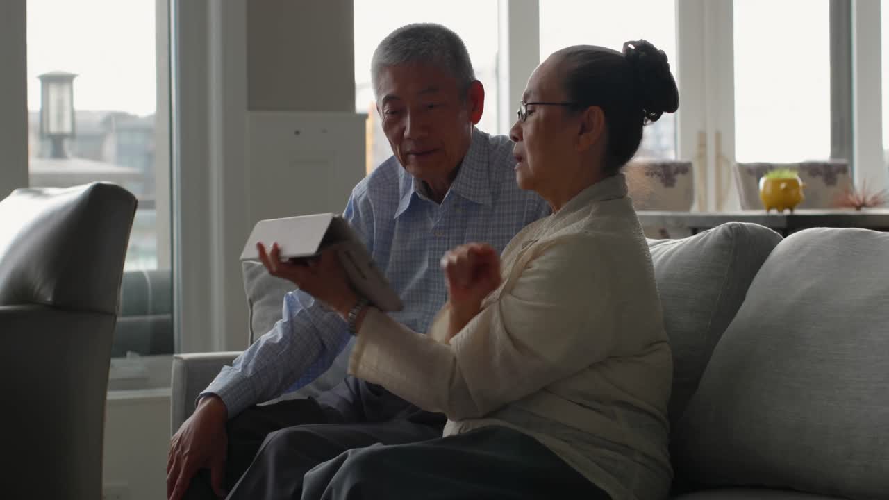 快適な自宅でデジタルタブレットについて話し合う高齢のアジア人夫婦（側面）4K