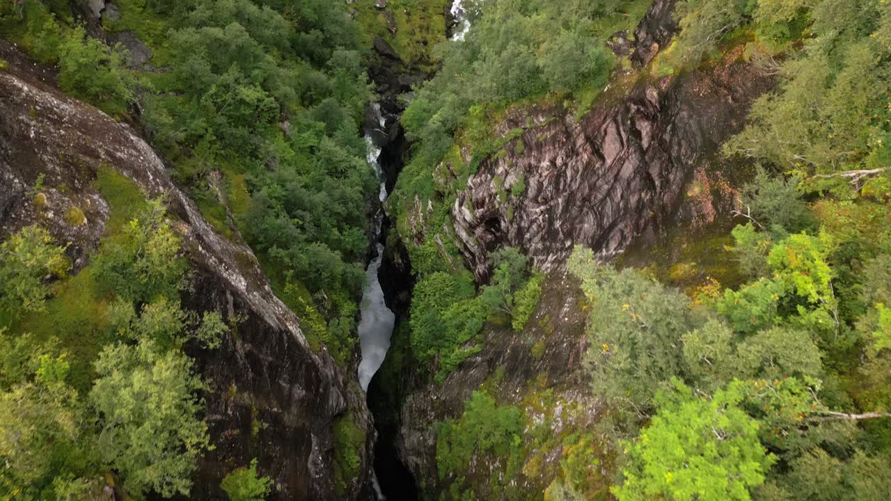Řeka protéká skalní štěrbinou v zeleném lese, Norsko, Evropa, dron.