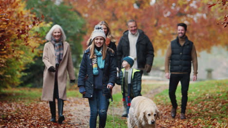 smiling multi-generation family with dog walking along path through autumn countryside together