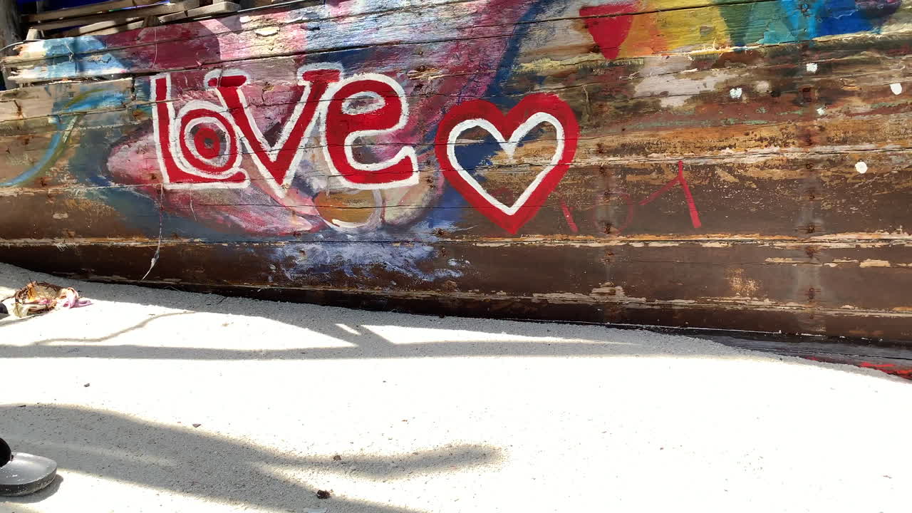 Riprese ravvicinate della parola Amore con una forma a cuore scritta in rosso sul legno e sabbia bianca in primo piano.