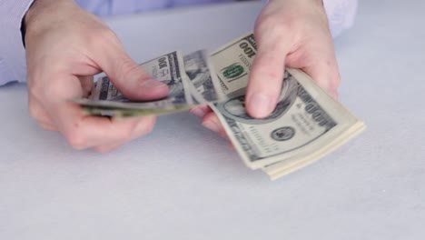 man counting one-hundred-dollar bills in the table