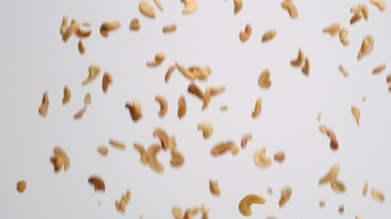 Roasted and salted cashew halves falling in slow motion on white backdrop