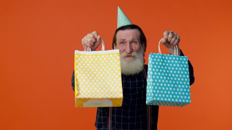 elderly bearded man showing shopping bags, advertising discounts, looking amazed with low prices