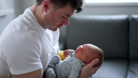 little newborn boy is crying in dad's hands. father tries to sooth his child waving him.