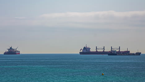 Enormes-Buques-De-Carga-Industriales-En-El-Mar,-Pequeños-Barcos-Pasando,-Timelapse