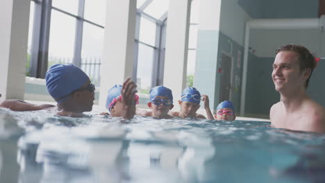 male swimming coach giving boy holding float lesson in pool